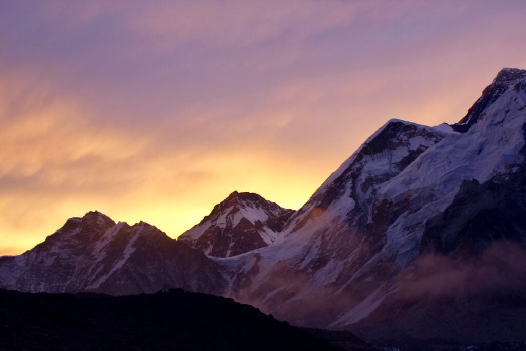 A pink, purple, and yellow sunrise over purple-tinted, snowy mountain peaks