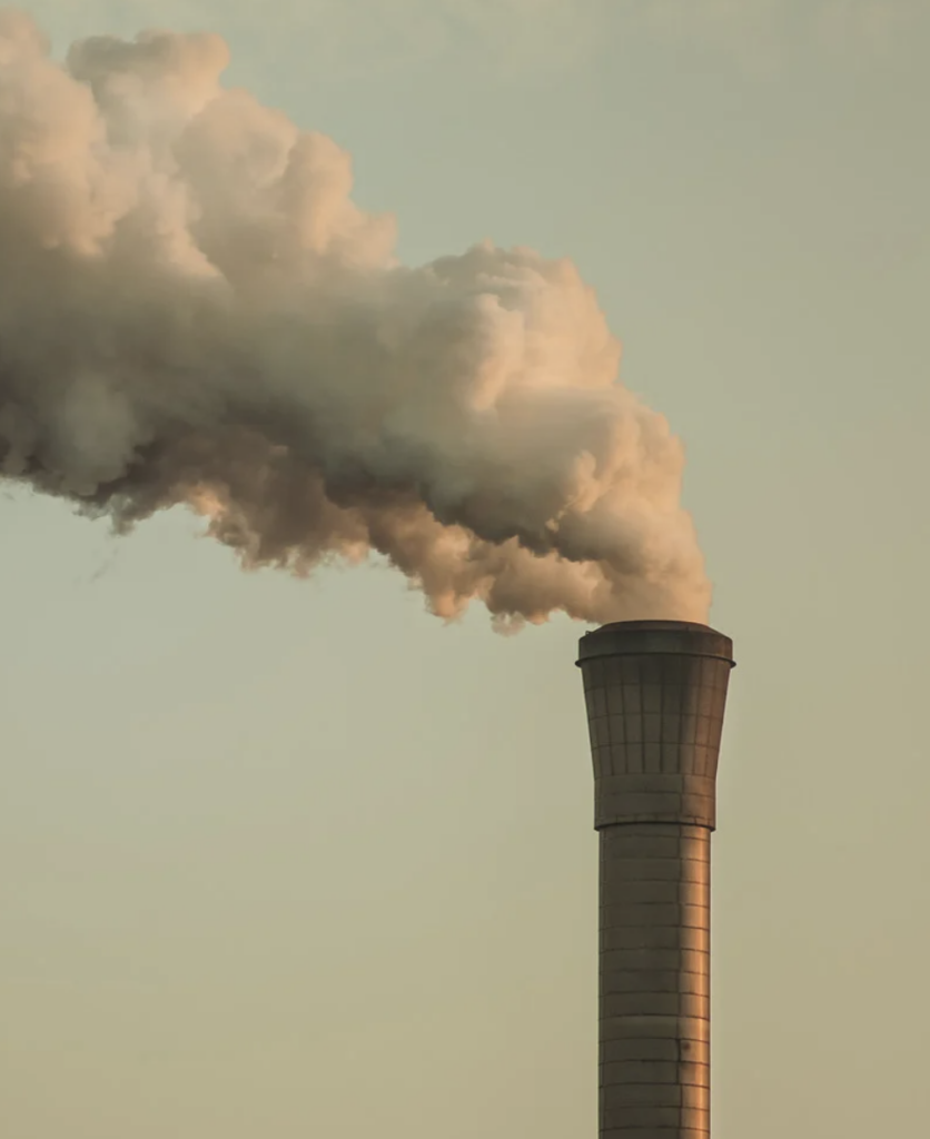 A photograph of a smokestack against a green-blue sky billowing thick white smoke