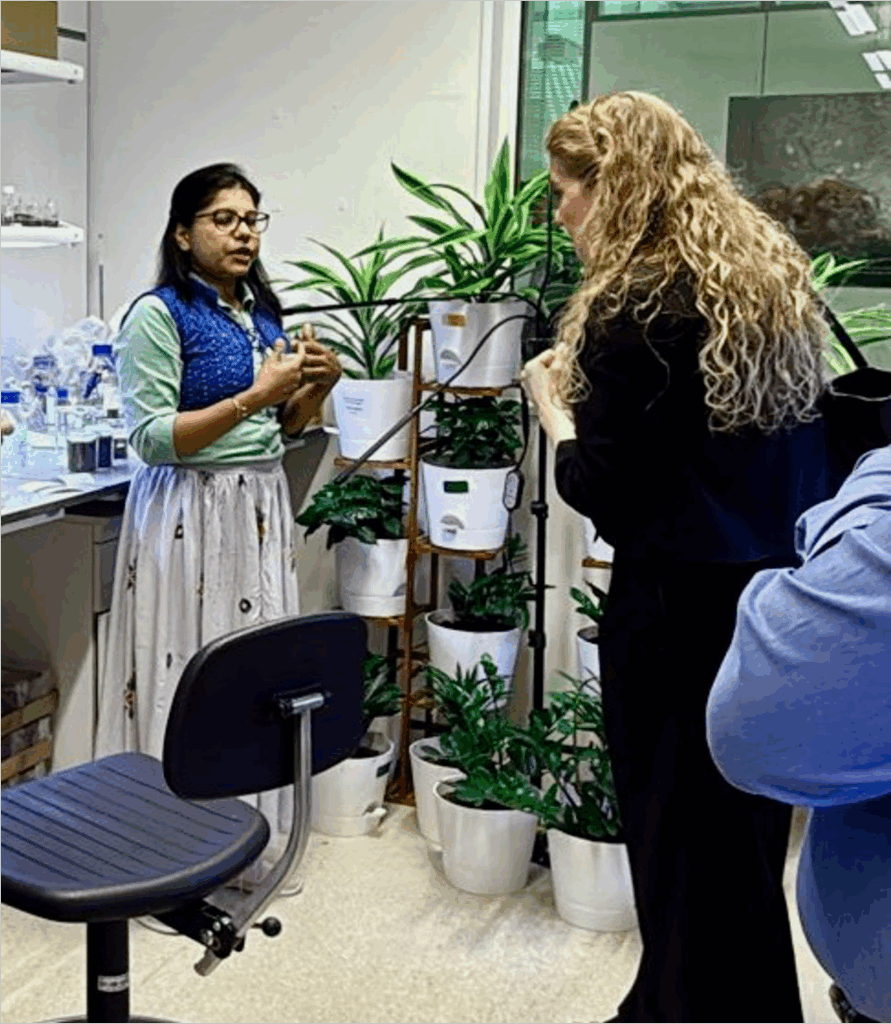 2 women in conversation in a lab standing in front of potted plants and scientific lab equipment